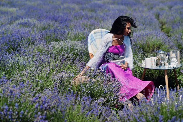 La bella ragazza indiana indossa l'abito tradizionale indiano del saree che si siede nel campo viola della lavanda con l'arredamento