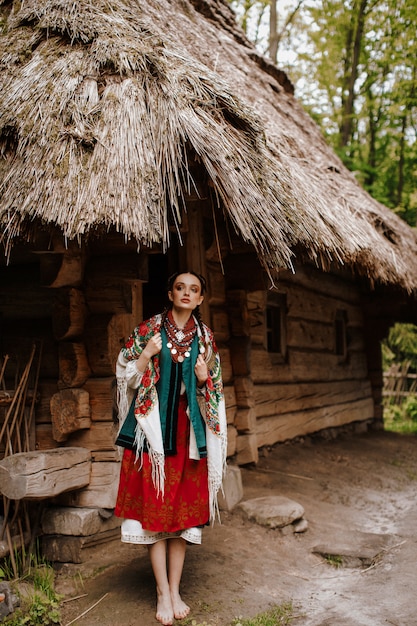 La bella ragazza posa sui cortili vicino alla casa in un vestito ucraino tradizionale