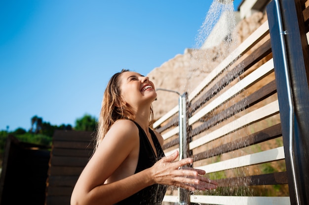 La bella ragazza si è vestita in costume da bagno che fa una doccia sulla spiaggia