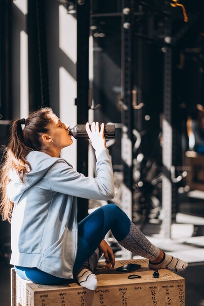 La bella ragazza stava bevendo acqua da una bottiglia di plastica, calda mattina di sole dentro la stanza