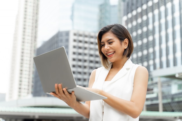 La bella ragazza sveglia che sorride in donna di affari copre facendo uso del computer portatile