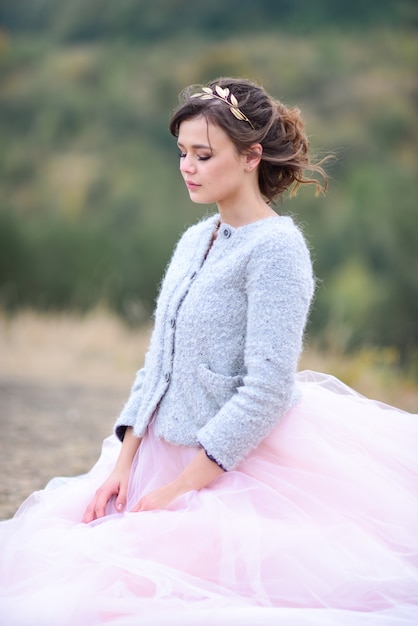 La bella sposa in vestito rosa e giacca blu si leva in piedi da qualche parte in una foresta