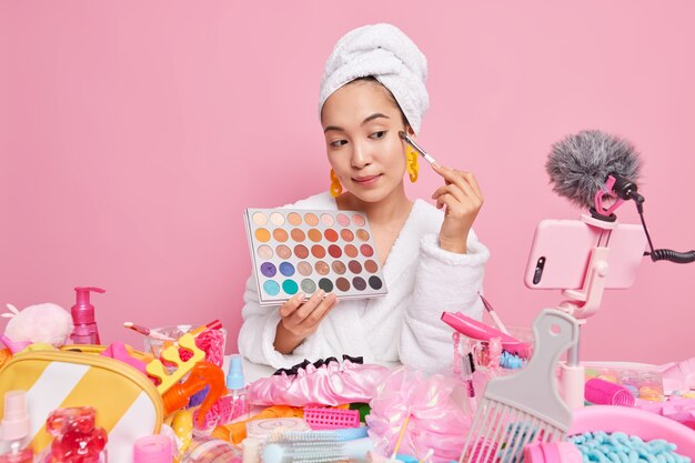 La blogger di bellezza professionale per donna trasmette video in streaming sul trucco applica un'ombra colorata con un pennello cosmetico tiene i record della tavolozza del corso di bellezza online