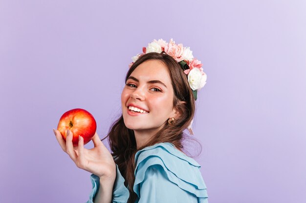 La bruna con le rose tra i capelli sta tenendo la mela rossa. Closeup ritratto di ragazza nell'immagine della moderna Biancaneve.