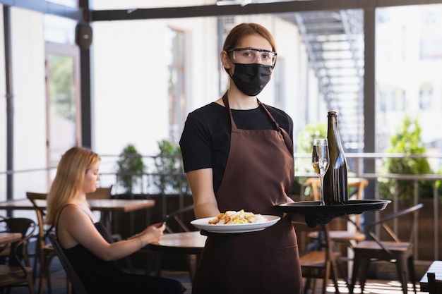 la cameriera lavora in un ristorante con una mascherina medica, guanti durante la pandemia di coronavirus
