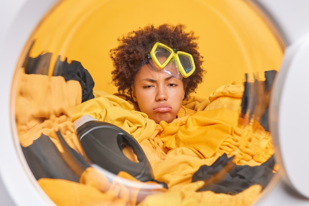 La casalinga della donna dai capelli ricci stanca e assonnata sembra oberata di lavoro mentre lava sepolta nel bucato