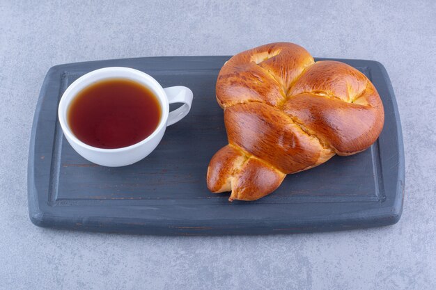 La colazione che serve di tè e panino dolce su una tavola su una superficie di marmo