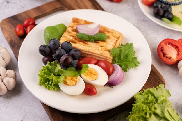 La colazione comprende pane, uova sode, condimento per insalata di uva nera, pomodori e cipolle affettate.