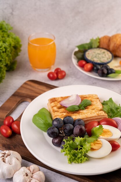 La colazione comprende pane, uova sode, condimento per insalata di uva nera, pomodori e cipolle affettate.