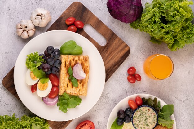 La colazione comprende pane, uova sode, condimento per insalata di uva nera, pomodori e cipolle affettate.