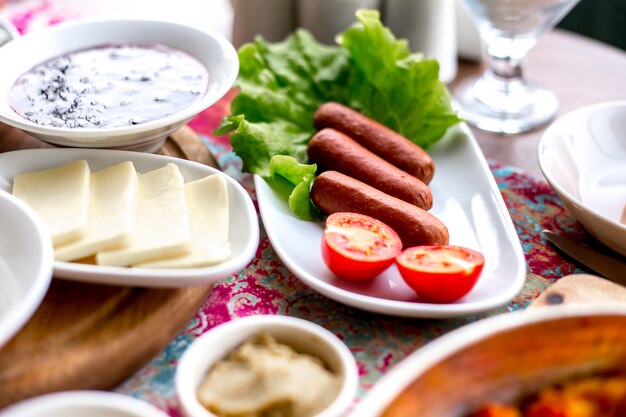 La colazione di vista laterale ha servito le salsiccie fritte tavola su una foglia dell'insalata con i pomodori ed il formaggio