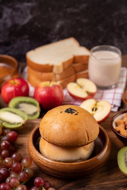 La colazione è composta da pane, mele, uva e kiwi su un tavolo di legno