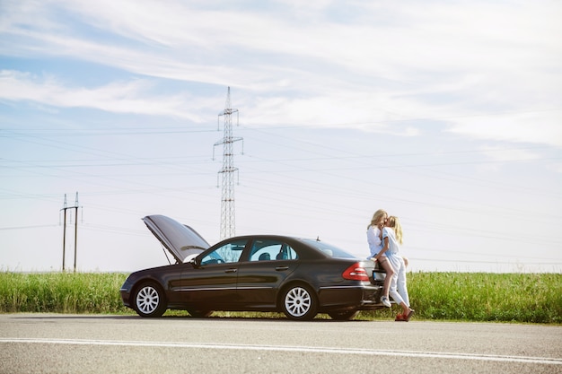 La coppia della giovane lesbica ha rotto la macchina mentre era in viaggio per riposarsi. Baci e coccole sul bagagliaio dell'auto. Relazione, guai sulla strada, vacanze, vacanze, concetto di luna di miele.