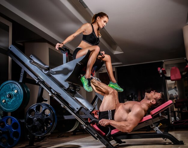 La coppia sportiva si sta allenando in palestra. Sollevatore pesi uomo che fa leg press con il suo allenatore.