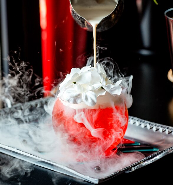 La crema viene versata in un bicchiere a forma rotonda con un cocktail rosso guarnito con crema e fiori