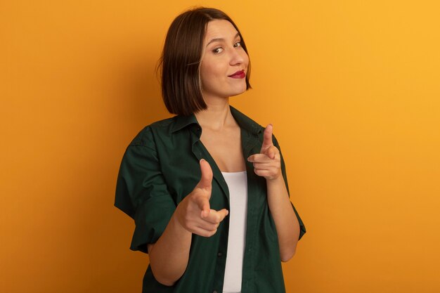 La donna abbastanza caucasica sicura guarda e indica la macchina fotografica con due mani sull'arancio