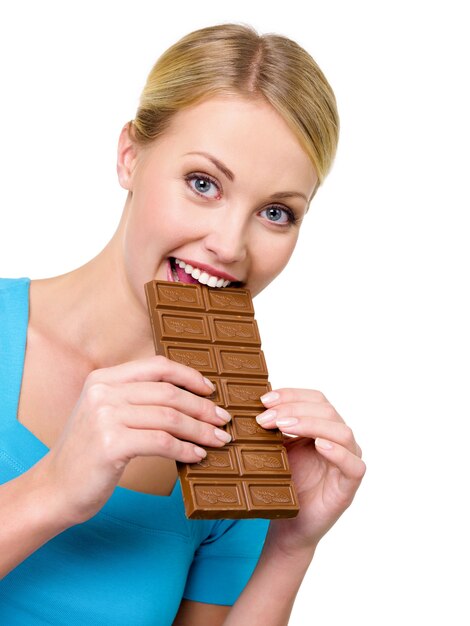 La donna abbastanza sorridente mangia il cioccolato nero dolce - su un bianco