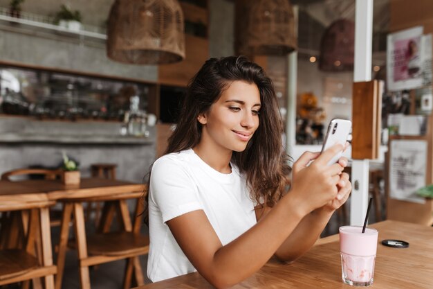 La donna abbronzata in maglietta bianca esamina lo schermo del telefono