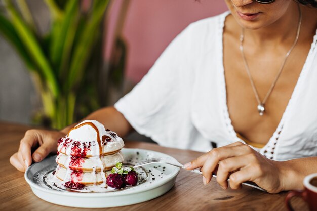 La donna abbronzata in maglietta bianca tiene la forchetta e mangia il dessert gustoso