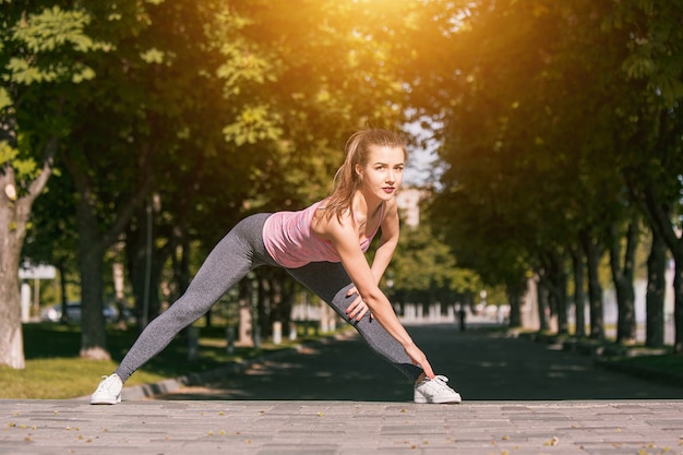 La donna adatta di forma fisica che fa l'allungamento si esercita all'aperto al parco