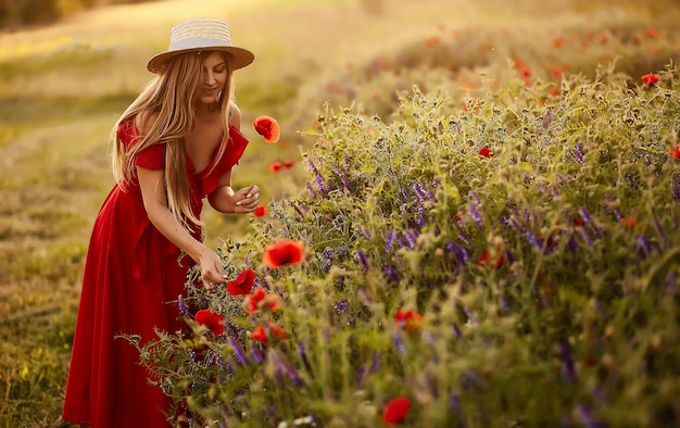 La donna affascinante cammina attraverso un campo verde con i papaveri nei raggi del sole di sera