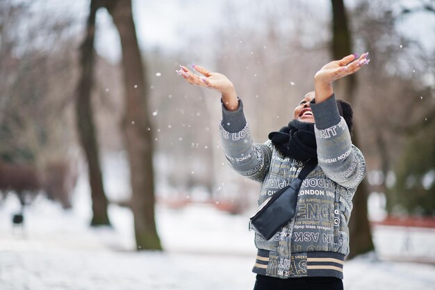 La donna africana indossa la sciarpa nera in posa nella giornata invernale in Europa, lancia la neve nell'aria