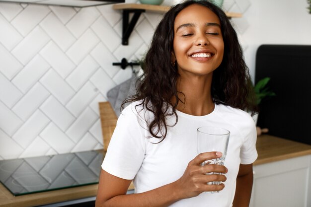 La donna afro graziosa tiene un bicchiere d'acqua e ha uno sguardo felice