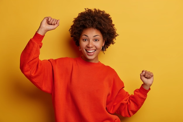 La donna afroamericana sorridente e gioiosa si diverte, esprime felicità, stringe i pugni, si diverte a fare festa con gli amici