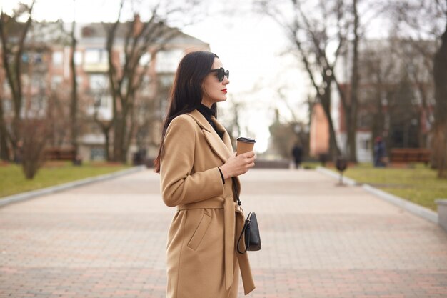 La donna alla moda del brunette passa il suo giorno libero avendo camminata in città.