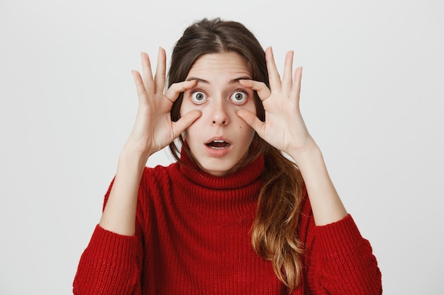 La donna allarga gli occhi con le mani, lo sguardo colpito