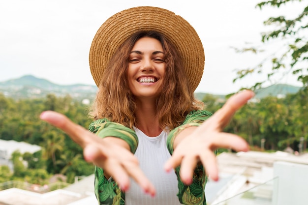 La donna allegra in cappello di paglia, divertendosi, allunga le mani alla macchina fotografica.