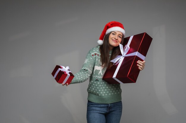 La donna allegra in maglione e cappello di natale si rallegra delle scatole con i suoi regali di natale