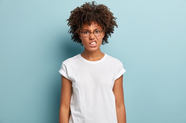 La donna arrabbiata e irritata ha un'acconciatura afro, stringe i denti per la rabbia, fissa con odio, aggrotta le sopracciglia