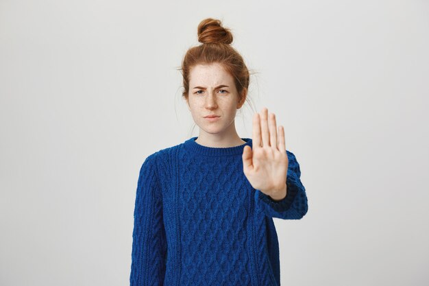 La donna arrabbiata e seria della testarossa allunga la mano per mostrare stop, limitare o proibire