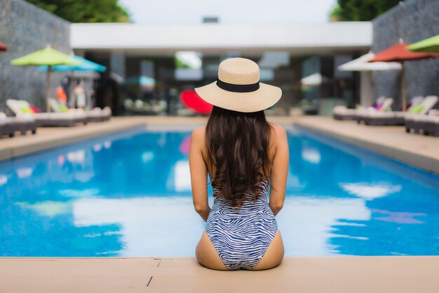 La donna asiatica del bello ritratto si rilassa il sorriso felice intorno alla piscina all'aperto