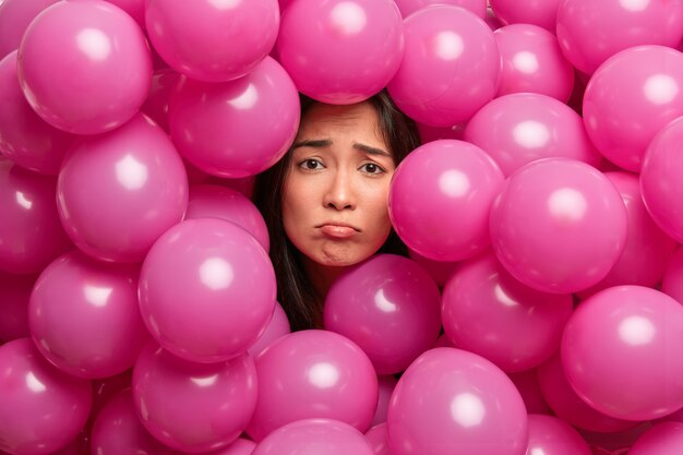 La donna asiatica miserabile scontenta sconvolta, circondata da palloncini rosa, ha un cattivo umore. Festa di compleanno noiosa. Concetto di emozioni negative