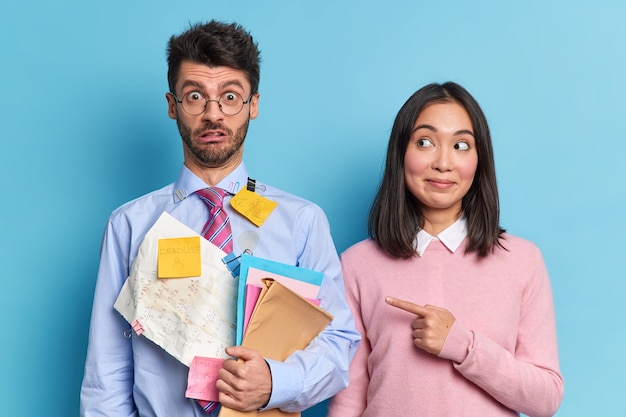 La donna asiatica soddisfatta indica il suo compagno di gruppo che ha un'espressione molto scioccata e si rende conto di avere una scadenza per prepararsi per la sessione piena di appunti adesivi per gli esami. Due studenti diversi al coperto