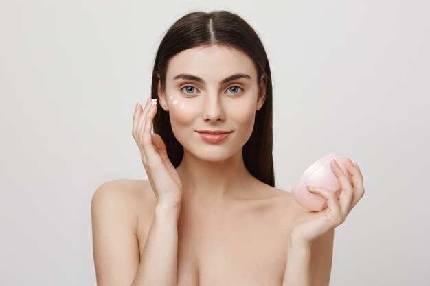 La donna attraente applica una crema per il viso, un prodotto antietà
