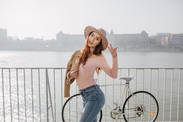 La donna attraente dello zenzero indossa la camicia rosa che gode della giornata di sole vicino al mare