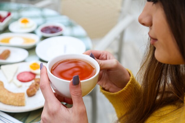 La donna beve il tè nero mentre la vista del primo piano della prima colazione