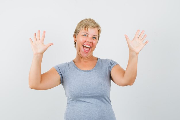 La donna bionda alza le mani e si rallegra in maglietta azzurra e sembra felice. vista frontale.