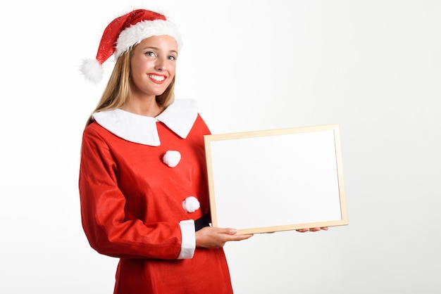 La donna bionda sorridente in vestiti di Santa Claus con la scheda bianca