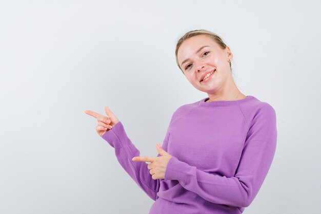 La donna bionda sorridente indica a sinistra con il suo indice su sfondo bianco