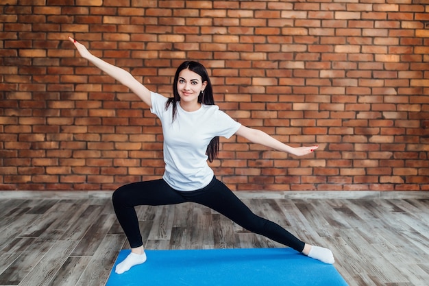 La donna castana esile pratica l'yoga in studio retroilluminato bianco.