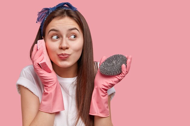 La donna caucasica positiva finge di parlare al telefono cellulare, tiene la spugna vicino all'orecchio, vestita in abiti casual