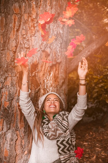 La donna che getta le foglie di autunno si avvicina all&#39;albero