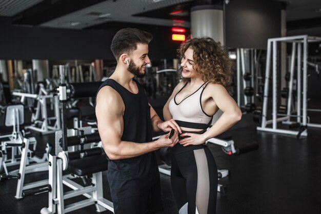 La donna che indossa lo sport indossa con la cintura e il suo personal trainer durante l'allenamento in palestra