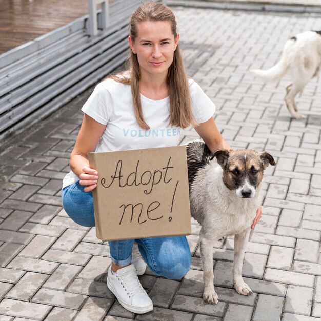 La donna che posa con il cane e che tiene mi adotta il segno per animale domestico