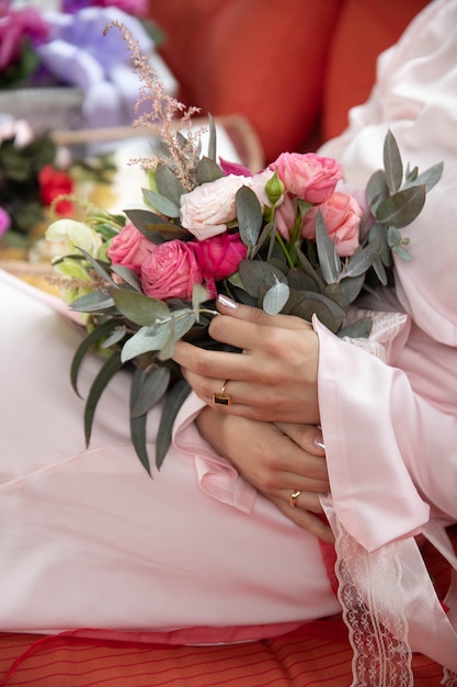 La donna che si siede e che tiene le nozze fiorisce nella sala in vestito rosa lungo e talloni rossi.