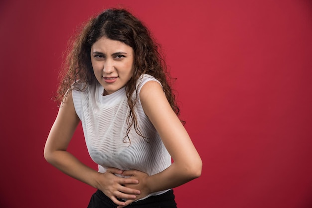 La donna con dolore sta tenendo la sua pancia dolorante sul rosso.